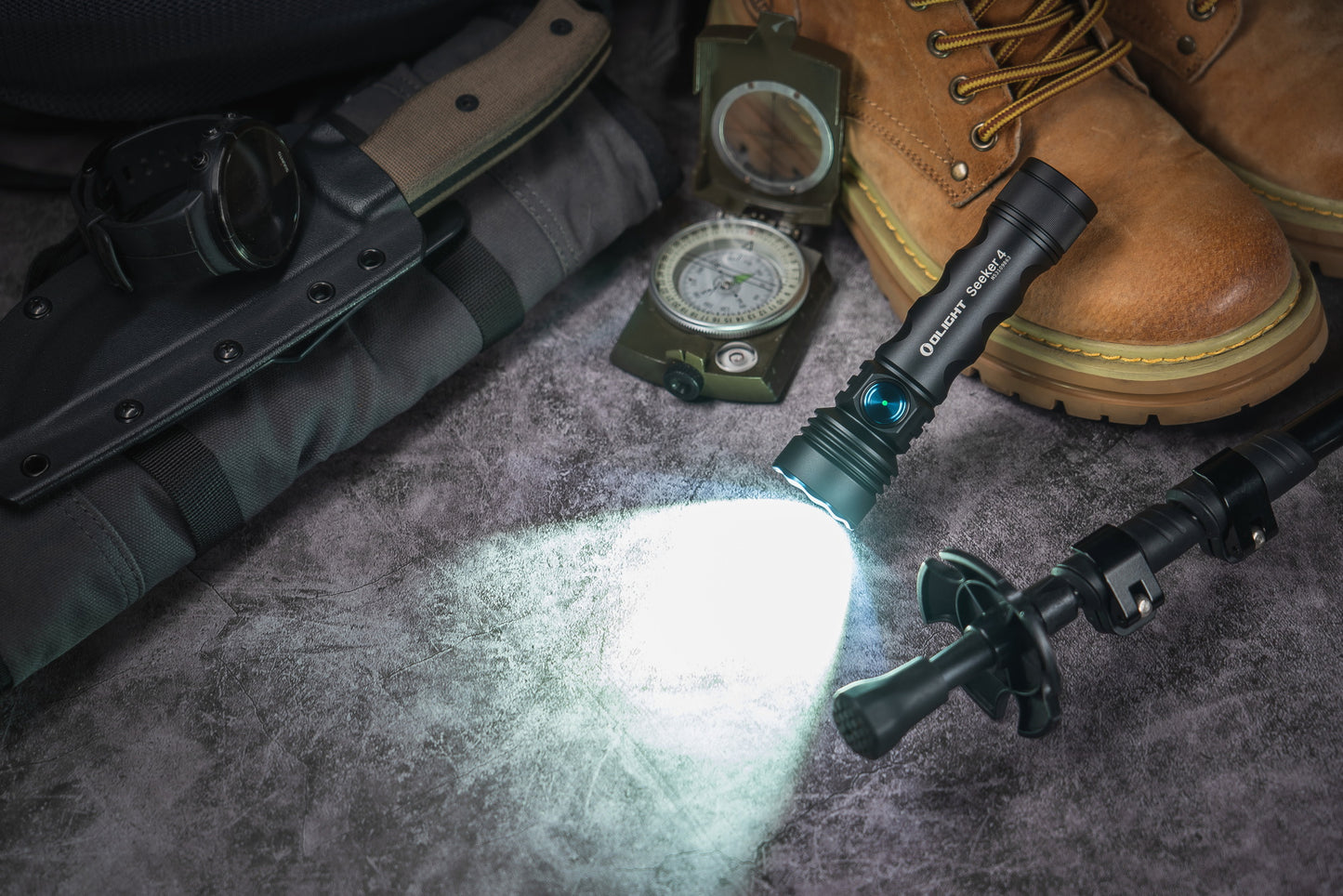 Flashlight illuminating a rugged outdoor setting with boots, compass, and knife.